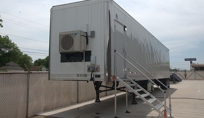 A white trailer-mounted mobile shooting range with an attached aluminum staircase