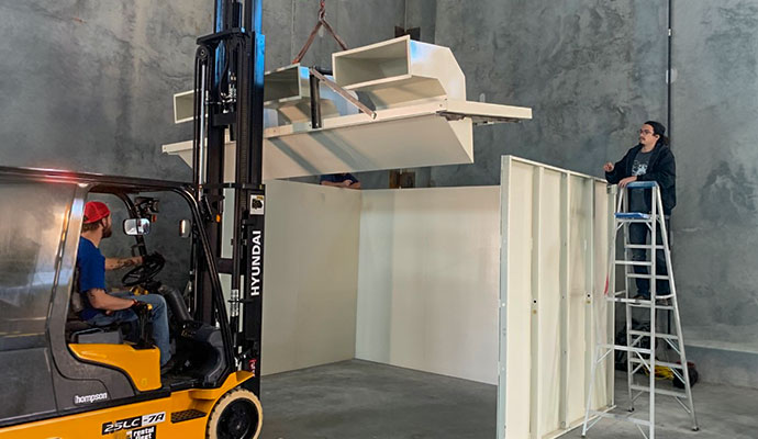 Technicians using a forklift and ladder to assemble panelized shooting range wall sections