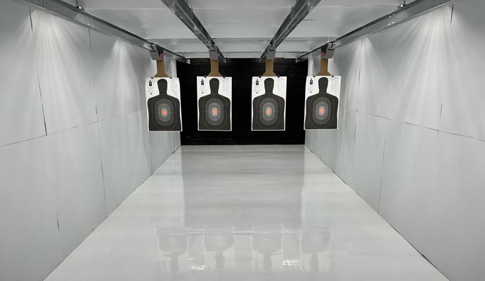 A clean, white indoor firing range with four automated silhouette targets suspended from a ceiling track system