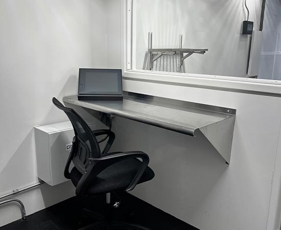 Interior of a white containerized structure, featuring a stainless steel desk with a touchscreen monitor